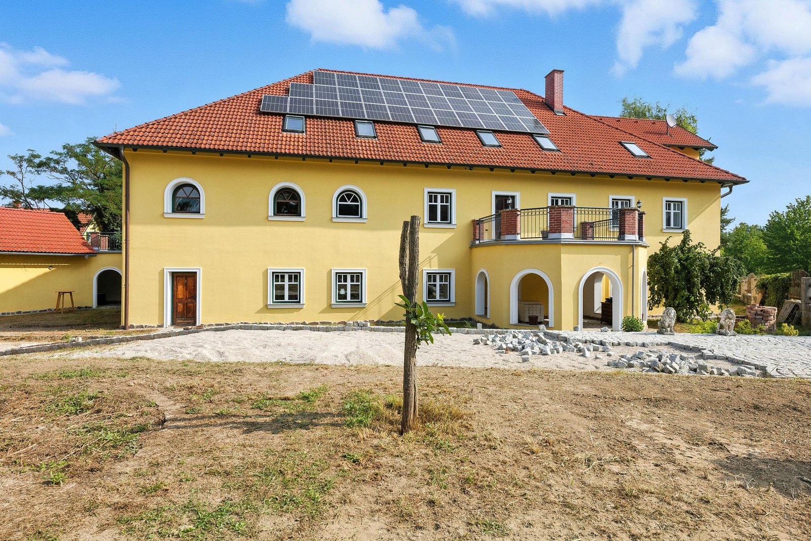 Frontaler Blick auf das Hauptgebäude mit Arkaden, Balkon und gelber Fassade